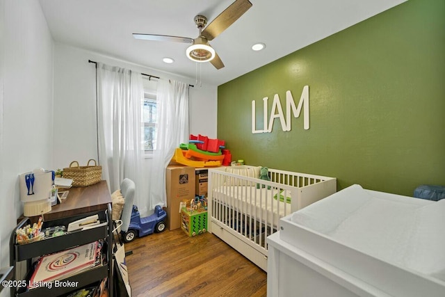 bedroom featuring ceiling fan, a nursery area, wood finished floors, and recessed lighting