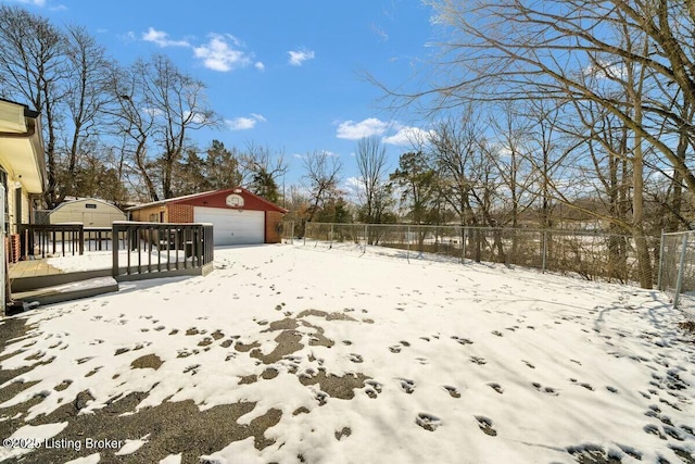 snowy yard featuring an outbuilding, fence, and a garage