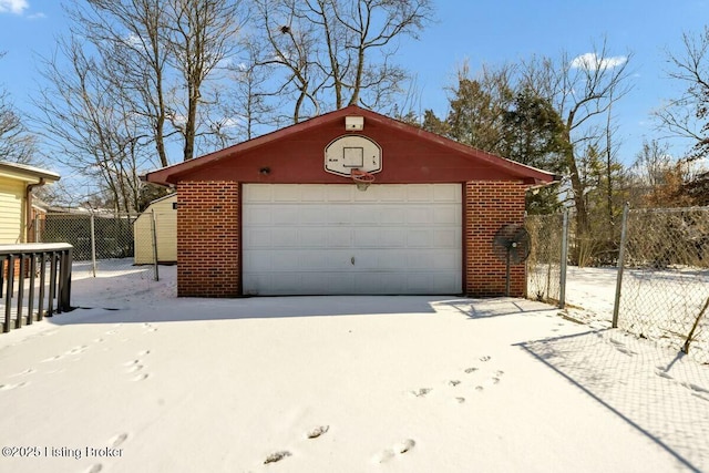 snow covered garage featuring a detached garage and fence