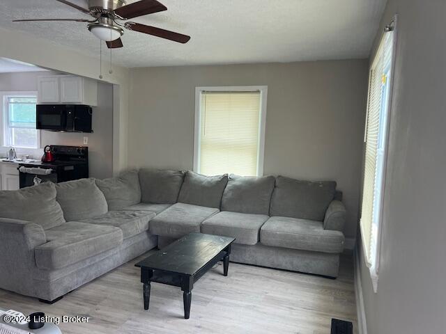 living room featuring ceiling fan, a textured ceiling, and light wood-type flooring