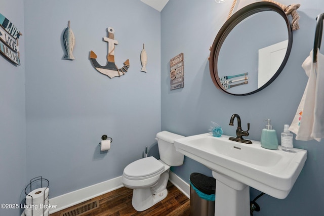 half bath featuring toilet, baseboards, visible vents, and wood finished floors