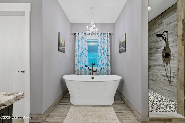 full bath featuring an inviting chandelier, a freestanding bath, tiled shower, and wood finished floors