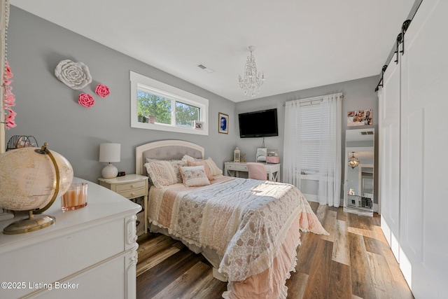 bedroom with a barn door, dark wood finished floors, visible vents, and a notable chandelier