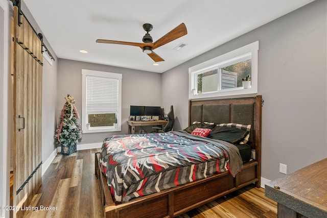 bedroom featuring a barn door, multiple windows, baseboards, and wood finished floors