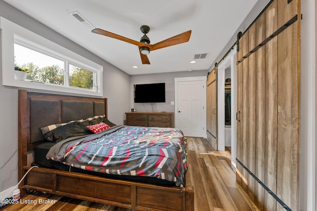 bedroom featuring ceiling fan, a barn door, wood finished floors, and visible vents