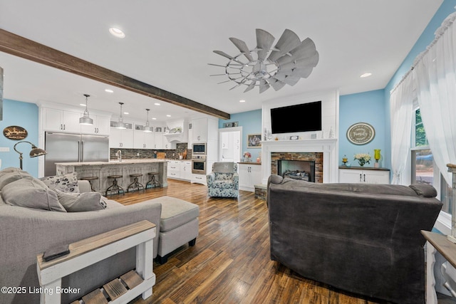 living area with dark wood-type flooring, recessed lighting, beam ceiling, and a fireplace