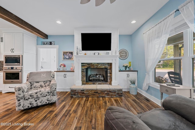 living room featuring a stone fireplace, recessed lighting, wood finished floors, baseboards, and beamed ceiling