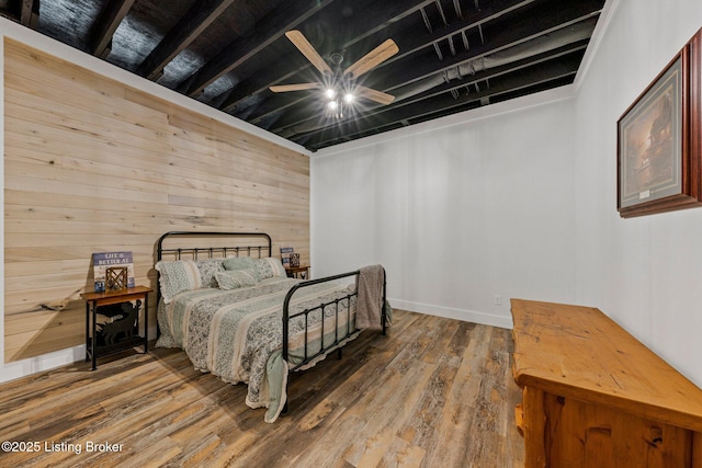 bedroom featuring a ceiling fan, beamed ceiling, wooden walls, and wood finished floors