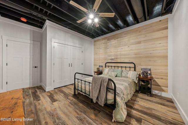 bedroom featuring a ceiling fan, a closet, wood walls, and wood finished floors