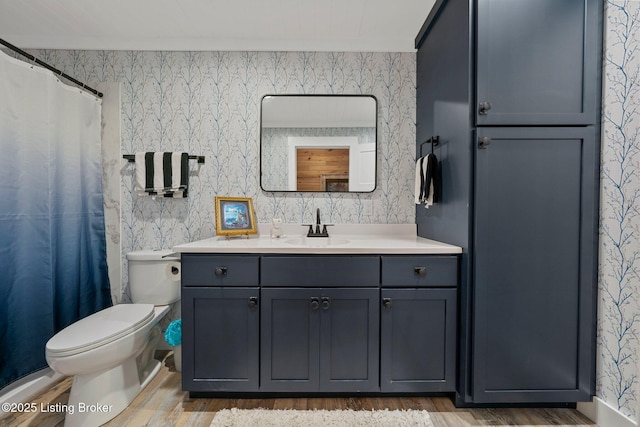 bathroom featuring wood finished floors, vanity, toilet, and wallpapered walls