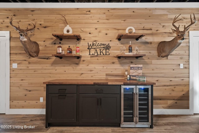 bar with a dry bar, wood walls, wood finished floors, beverage cooler, and baseboards