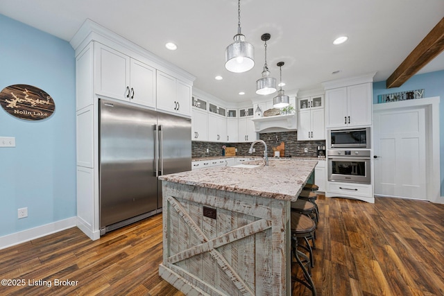 kitchen with built in appliances, a sink, backsplash, and glass insert cabinets