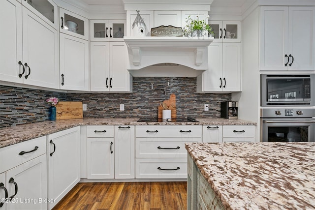 kitchen with dark wood-type flooring, glass insert cabinets, stainless steel appliances, and decorative backsplash