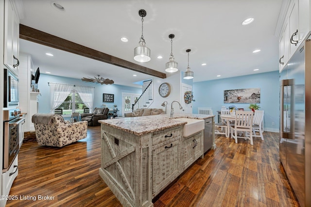 kitchen featuring light stone counters, beam ceiling, dark wood finished floors, stainless steel appliances, and a sink