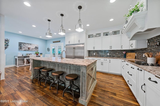 kitchen featuring glass insert cabinets, light stone counters, dark wood finished floors, and built in fridge