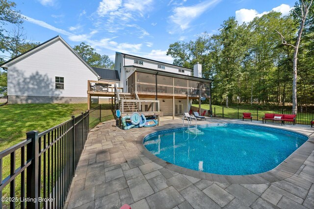 view of swimming pool with fence, a sunroom, a lawn, a fenced in pool, and a patio area