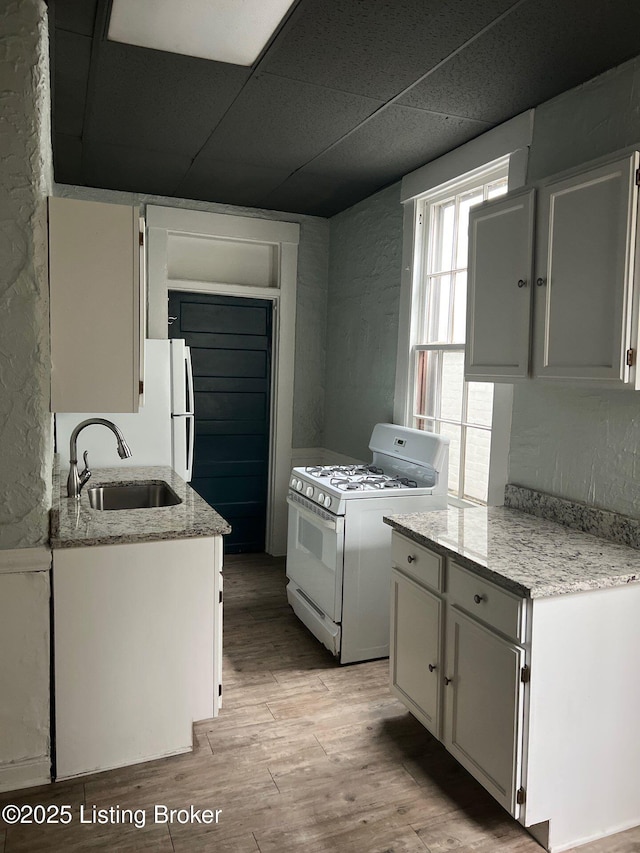 kitchen featuring sink, white appliances, a paneled ceiling, light hardwood / wood-style floors, and white cabinets