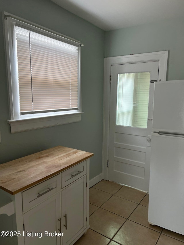 interior space featuring white cabinetry, a wealth of natural light, light tile patterned flooring, and white fridge