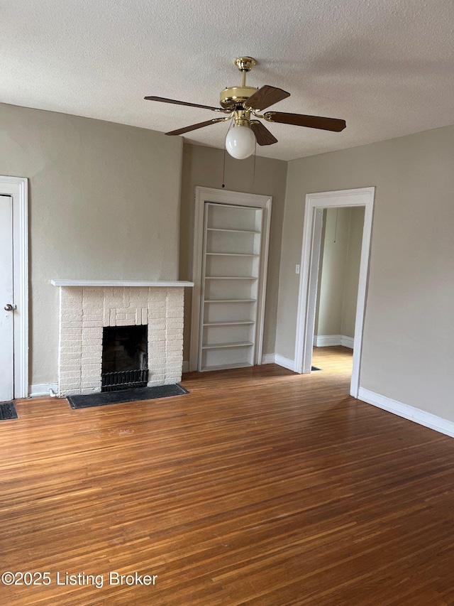 unfurnished living room with hardwood / wood-style flooring, ceiling fan, a brick fireplace, a textured ceiling, and built in shelves