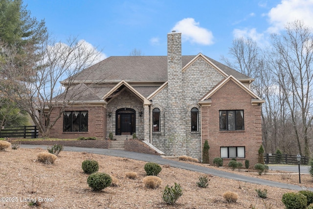 view of front facade with roof with shingles, brick siding, a chimney, and fence