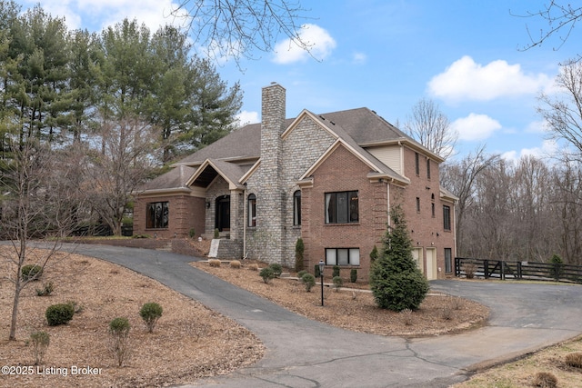 view of front of house with aphalt driveway, brick siding, a chimney, fence, and a garage