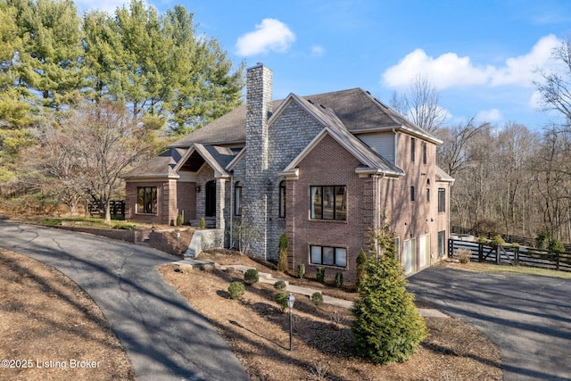 view of front of property featuring driveway, a garage, a chimney, fence, and brick siding