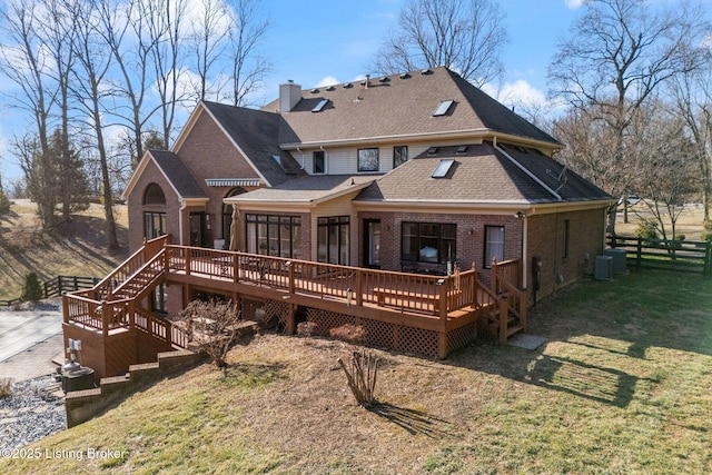 rear view of property featuring brick siding, fence, a lawn, and a wooden deck