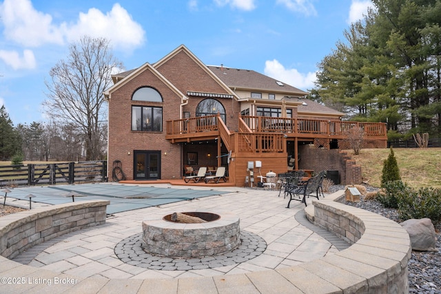 rear view of house with an outdoor fire pit, a wooden deck, stairs, french doors, and a patio area