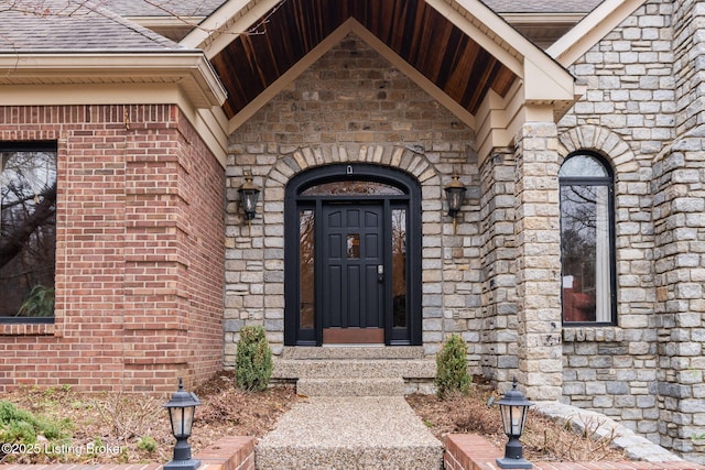 entrance to property featuring stone siding, a shingled roof, and brick siding