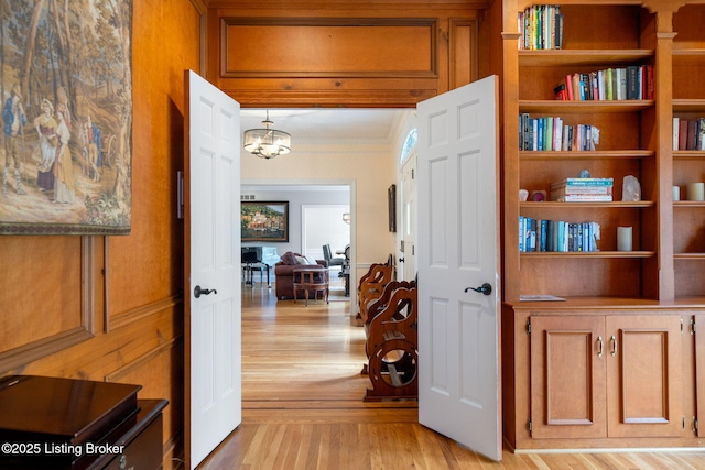 hall with a chandelier, crown molding, and light wood finished floors