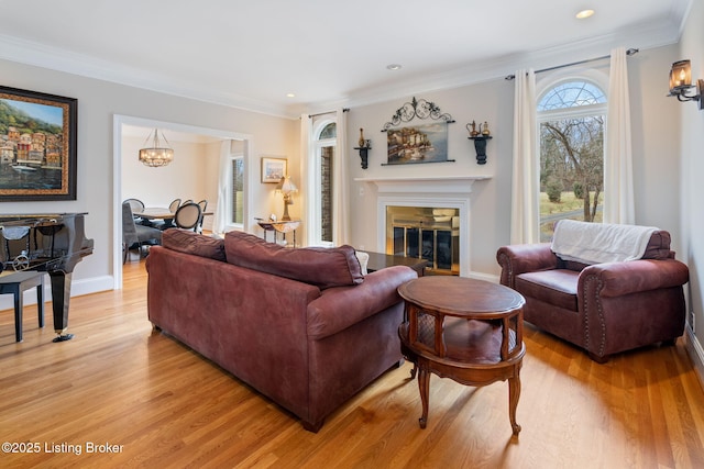 living area with baseboards, light wood-style floors, an inviting chandelier, a glass covered fireplace, and crown molding