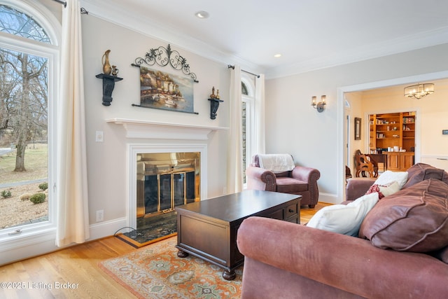 living room with light wood-style floors, a wealth of natural light, a glass covered fireplace, and crown molding