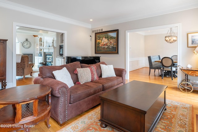 living room featuring light wood-style flooring, a fireplace, visible vents, and crown molding