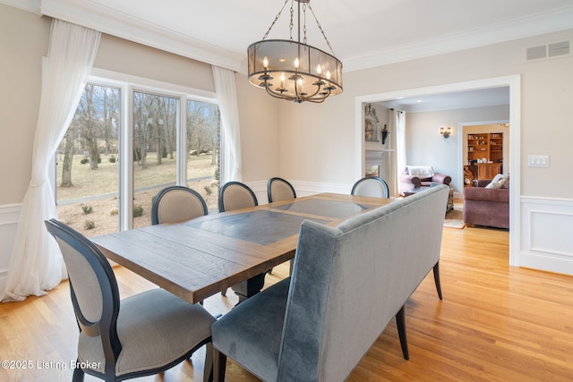 dining room featuring a wainscoted wall, visible vents, a decorative wall, ornamental molding, and light wood-style floors