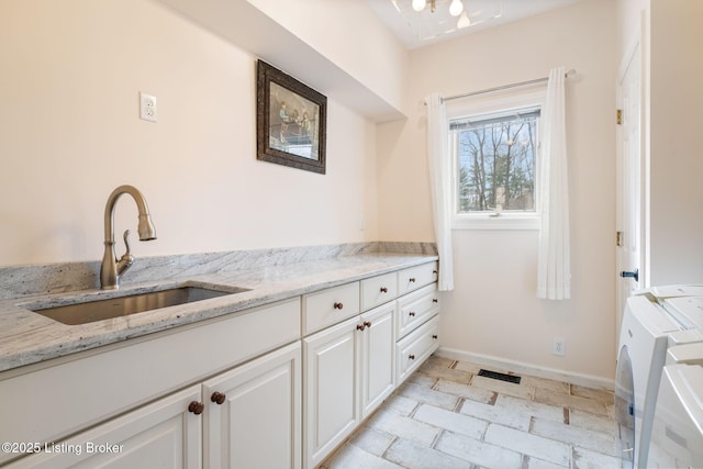 washroom with a sink, visible vents, baseboards, washer and dryer, and cabinet space