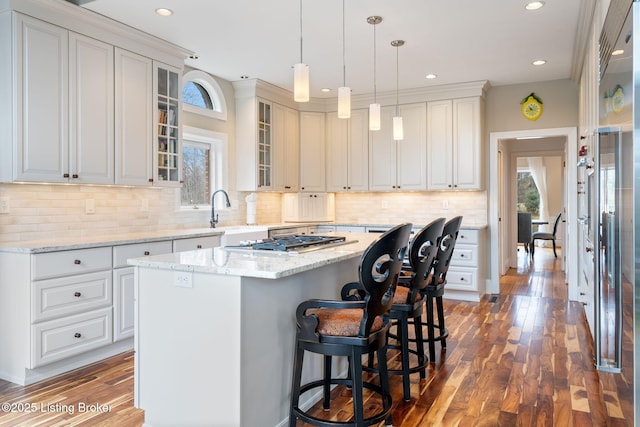 kitchen with glass insert cabinets, a center island, decorative light fixtures, and white cabinetry