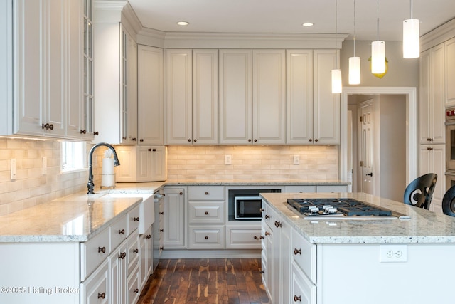 kitchen featuring light stone counters, stainless steel appliances, a sink, white cabinets, and pendant lighting