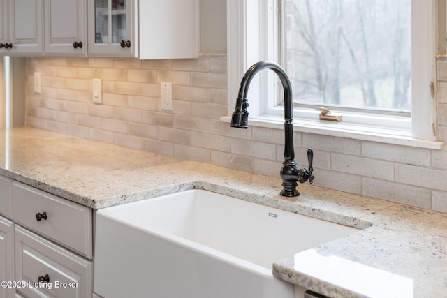 details with glass insert cabinets, white cabinetry, and light stone countertops