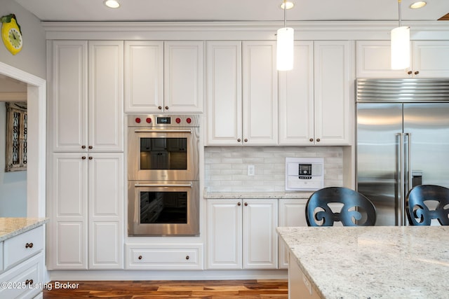 kitchen featuring hanging light fixtures, light stone countertops, white cabinetry, and appliances with stainless steel finishes