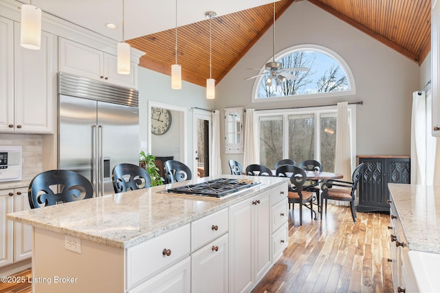 kitchen with wood finished floors, a kitchen island, white cabinetry, appliances with stainless steel finishes, and pendant lighting