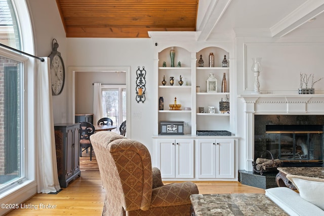 sitting room featuring wooden ceiling, built in features, light wood-type flooring, beamed ceiling, and a glass covered fireplace