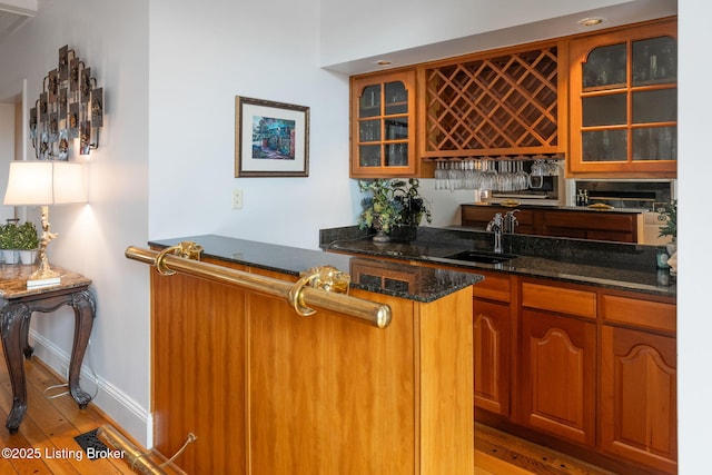 bar featuring light wood finished floors, baseboards, indoor wet bar, and a sink