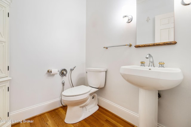 half bath with toilet, a sink, baseboards, and wood finished floors