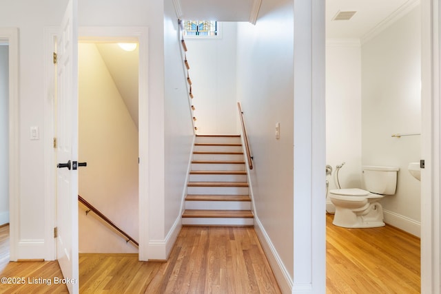 staircase featuring baseboards, visible vents, wood finished floors, and ornamental molding