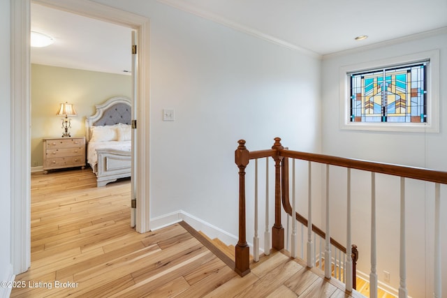 hallway with light wood-type flooring, baseboards, crown molding, and an upstairs landing