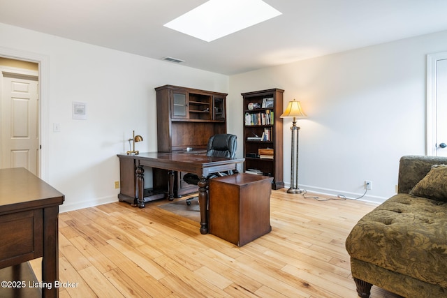 office space with a skylight, baseboards, visible vents, and light wood-style floors