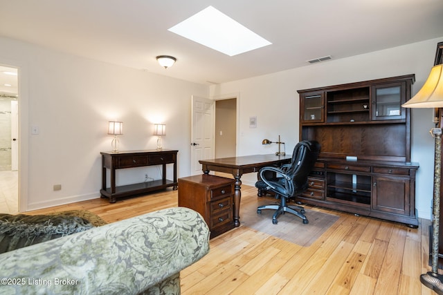 home office with a skylight, baseboards, visible vents, and light wood finished floors