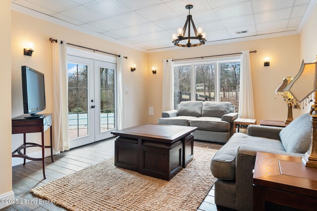 living room featuring french doors, crown molding, visible vents, an inviting chandelier, and light wood-type flooring