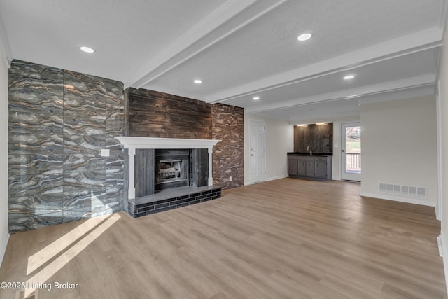 unfurnished living room featuring beamed ceiling, wood-type flooring, sink, and a textured ceiling