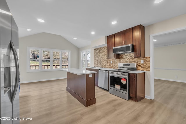 kitchen with vaulted ceiling, tasteful backsplash, a center island, light hardwood / wood-style floors, and stainless steel appliances